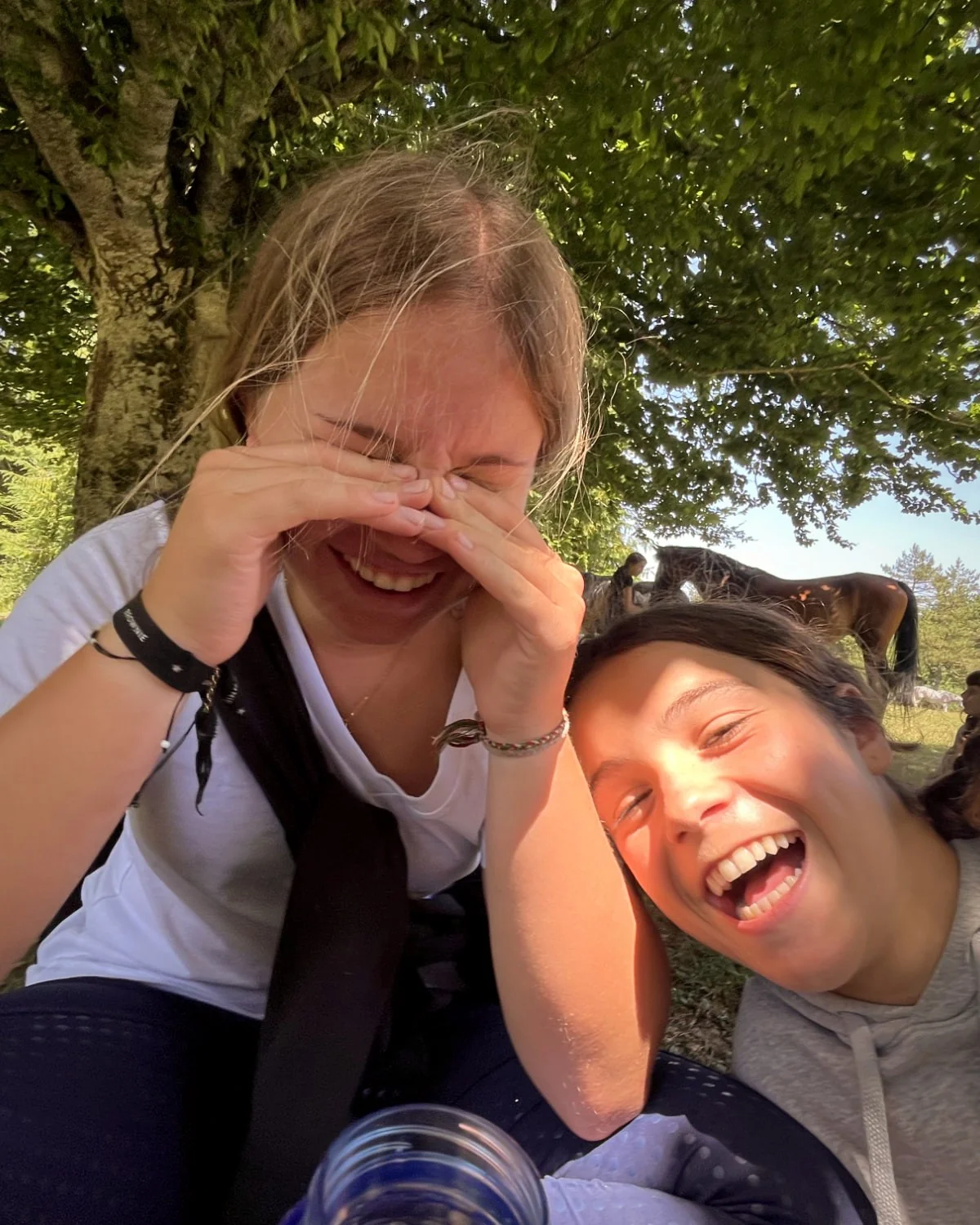 Dos amigas riendo bajo un árbol durante el campamento